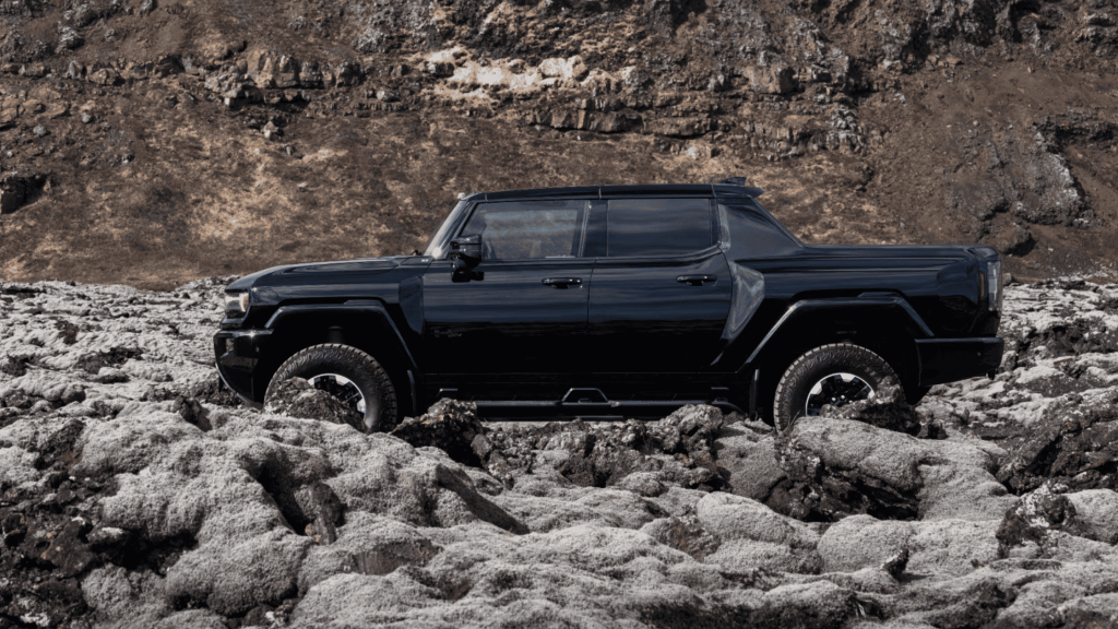 Side view of 2025 GMC Hummer EV Pickup in black driving over volcanic rocky terrain