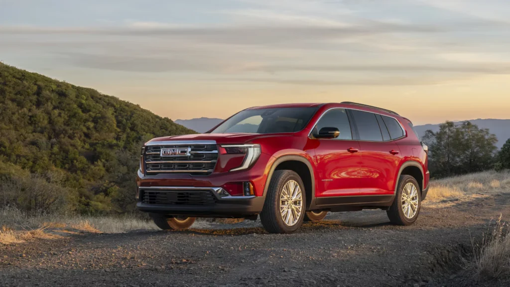 2025 GMC Acadia in red parked along a scenic mountain trail at sunset.