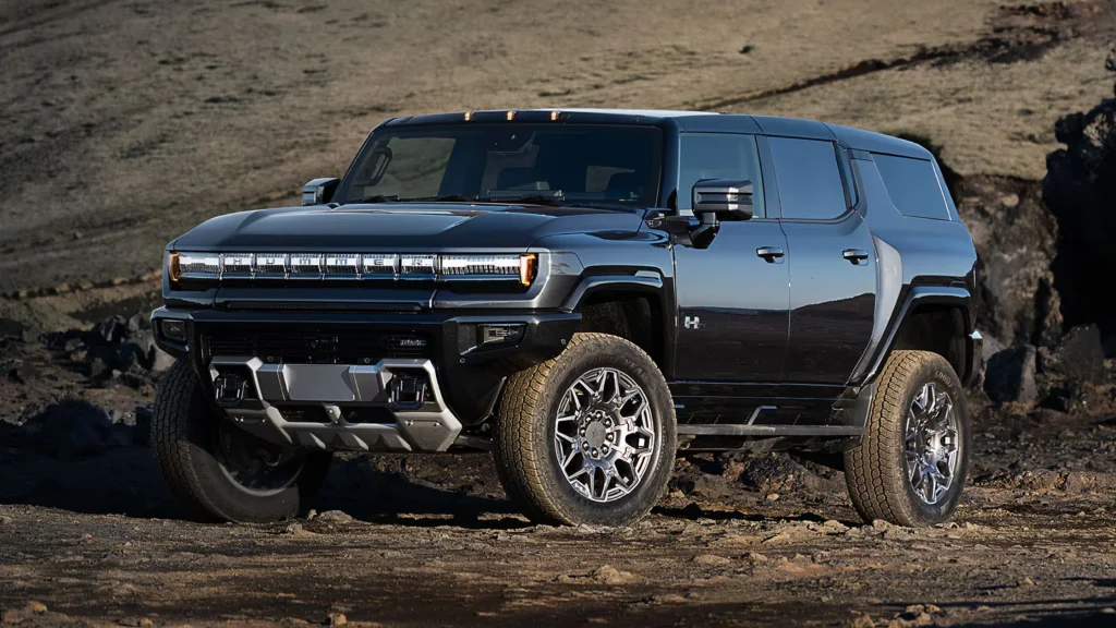 A black 2025 GMC Hummer EV SUV parked on rugged terrain, showcasing its bold front grille, wide stance, and off-road capabilities.
