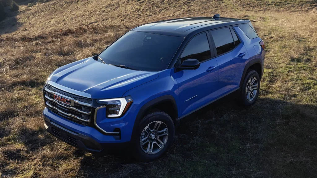 A blue 2025 GMC Terrain compact SUV positioned on grassy hills, emphasizing its athletic design and outdoor versatility.