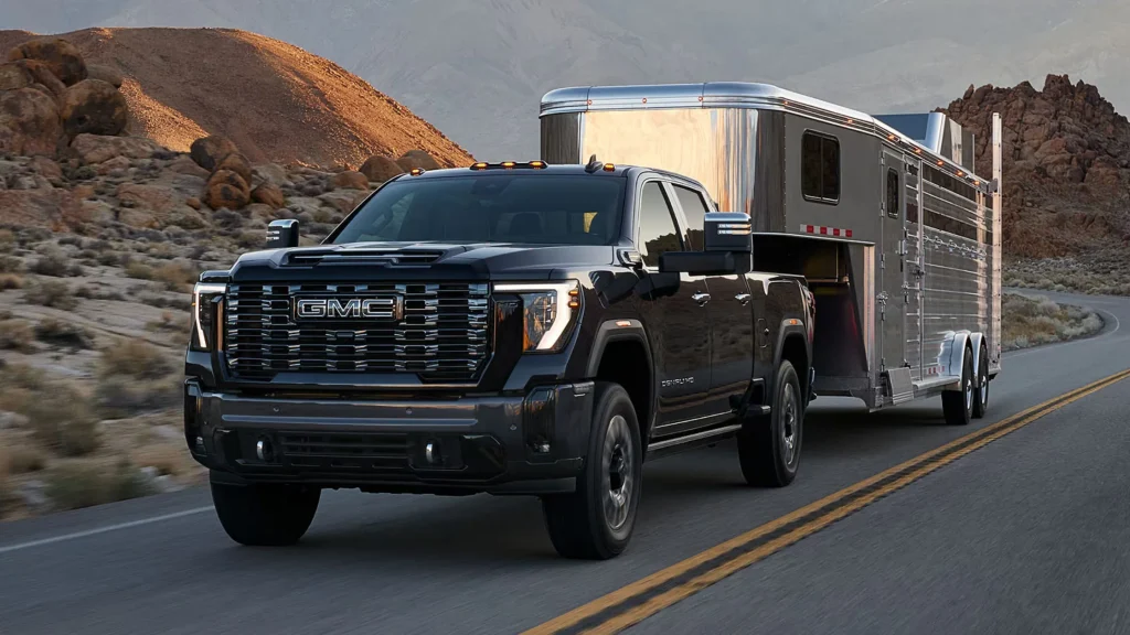 Front view of a black 2025 GMC Sierra 3500 HD towing a silver trailer on a desert road.