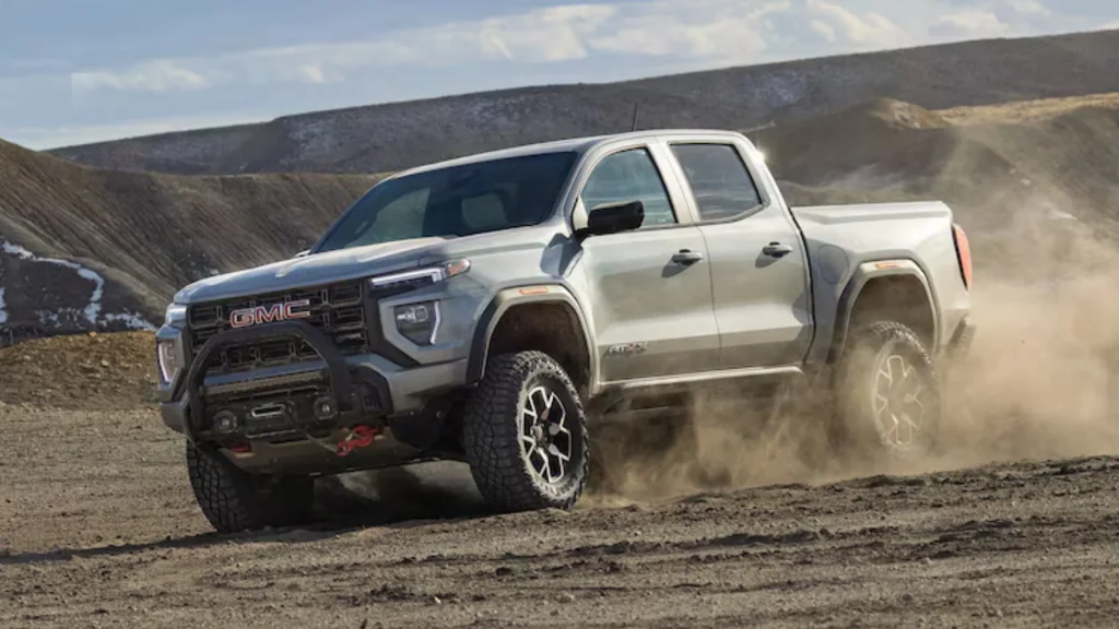 2026 GMC Canyon AT4X pickup kicking up dirt on rugged terrain with aggressive off-road tires.