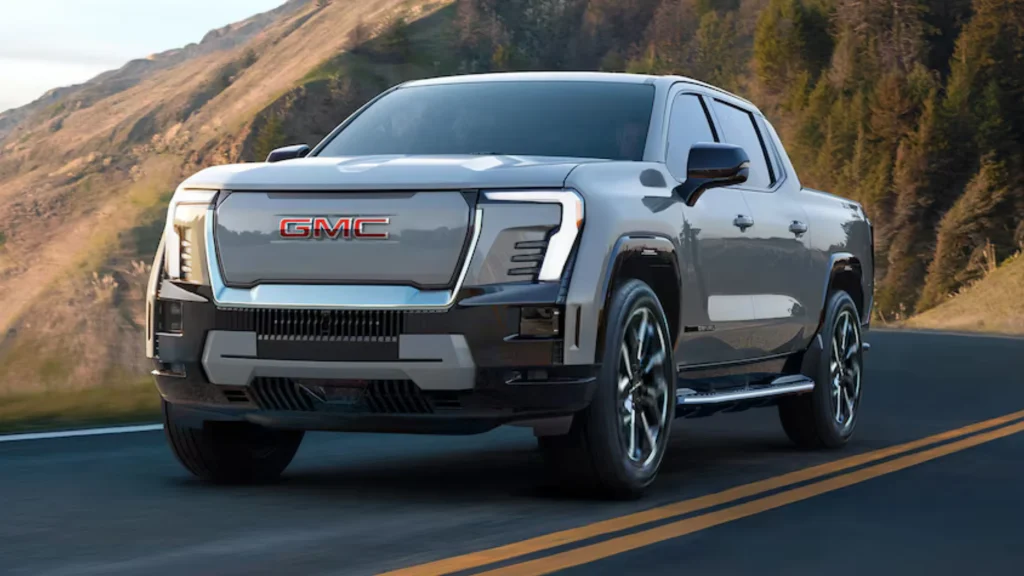 2026 GMC Sierra EV electric truck driving on a mountain road with bold front fascia and LED headlights.