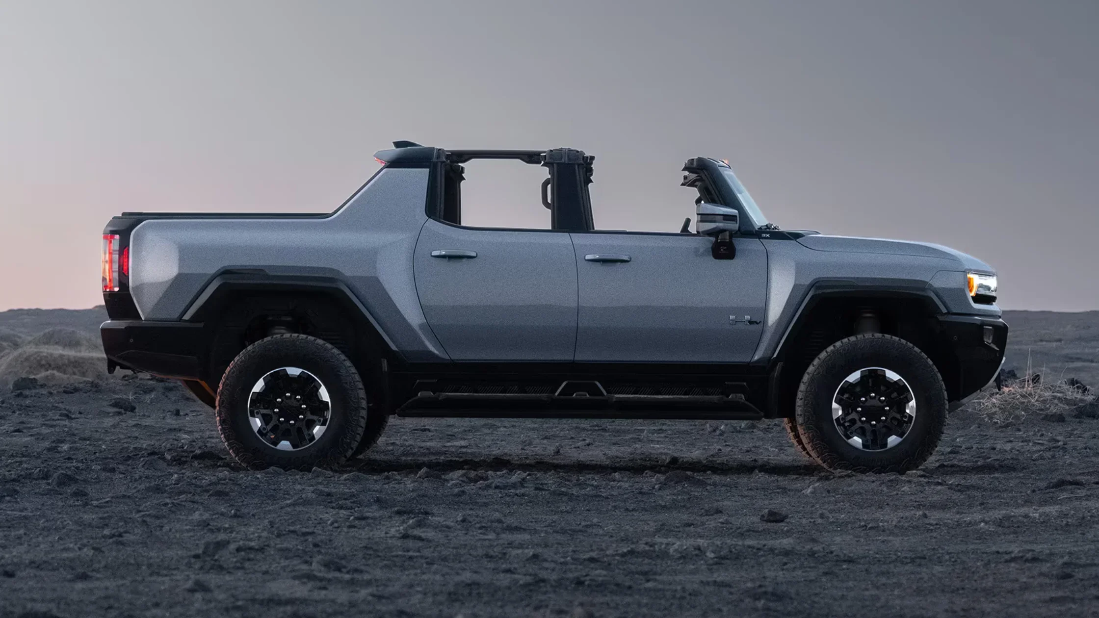 Side profile of 2025 Hummer EV SUV parked on rocky terrain with doors off and rugged wheels.