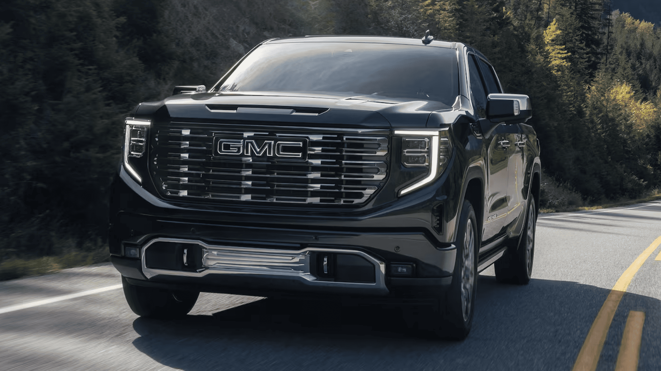 Front view of 2025 GMC Sierra 1500 driving on a curved road with distinctive chrome grille.