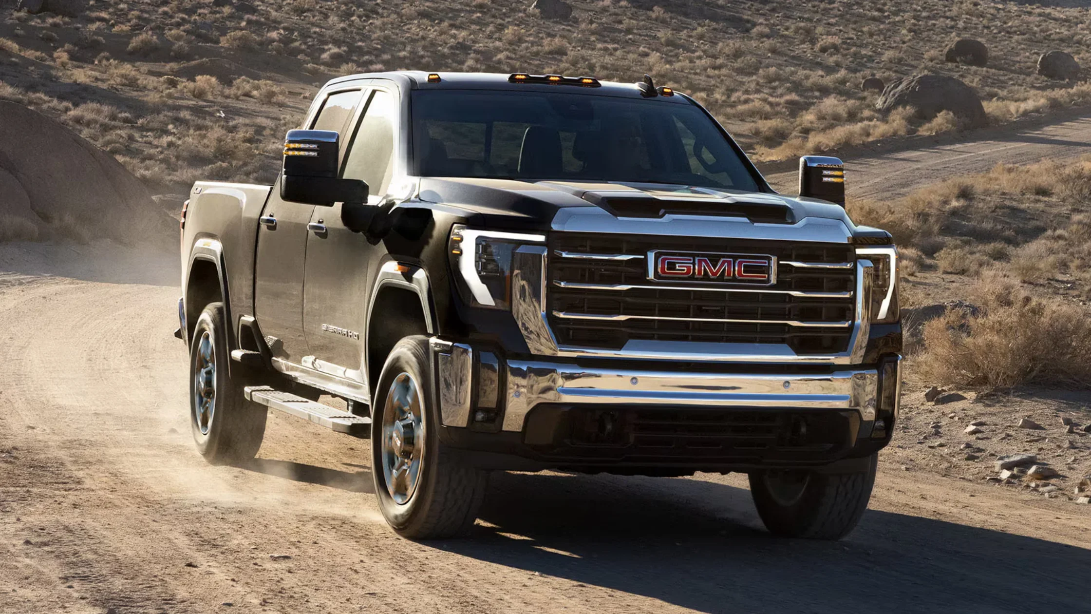 2025 GMC Sierra 3500 HD pickup driving on rugged desert trail with dust trailing behind.