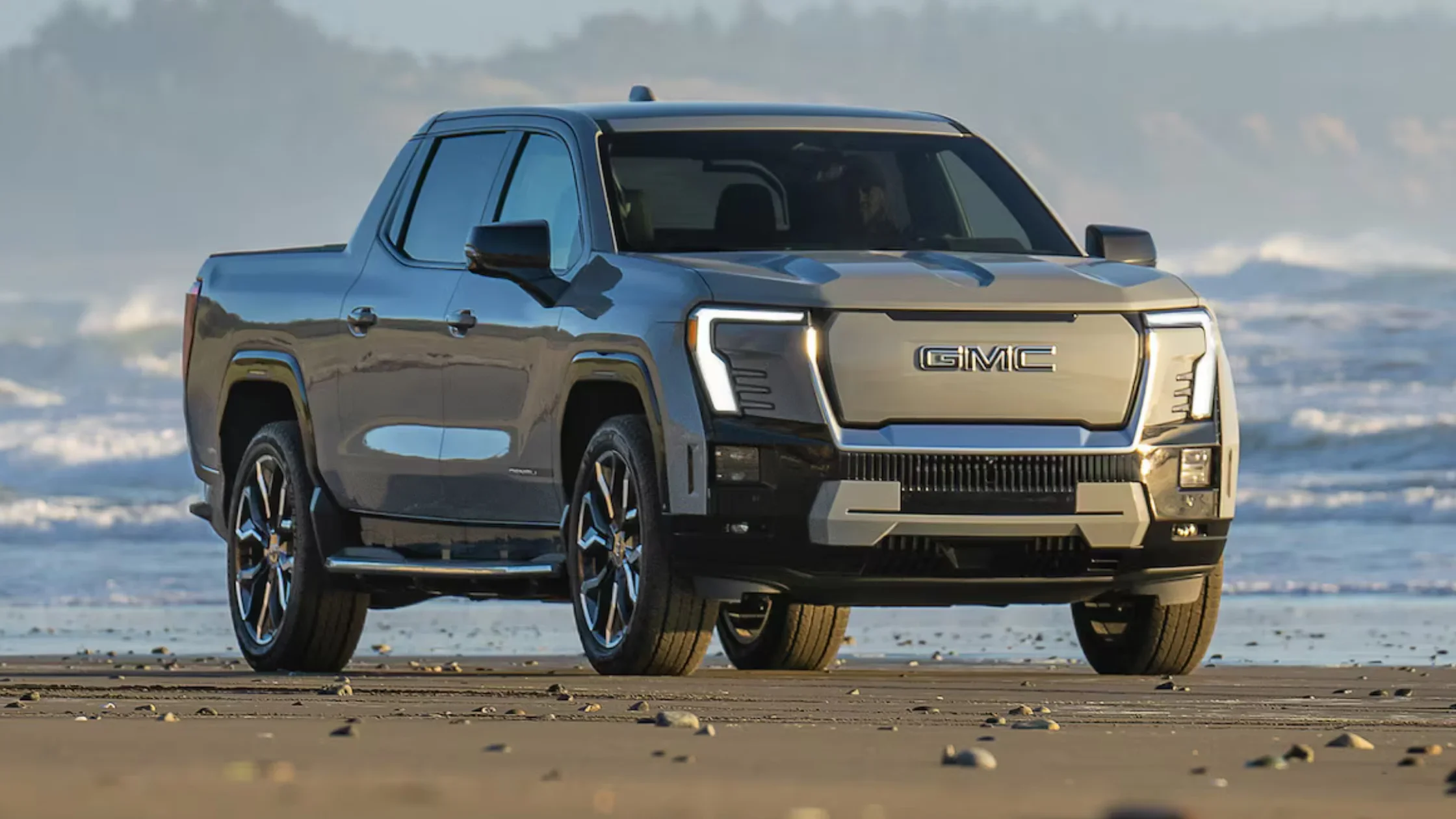 2025 GMC Sierra EV Denali Edition 1 parked on beach with ocean backdrop under soft light.