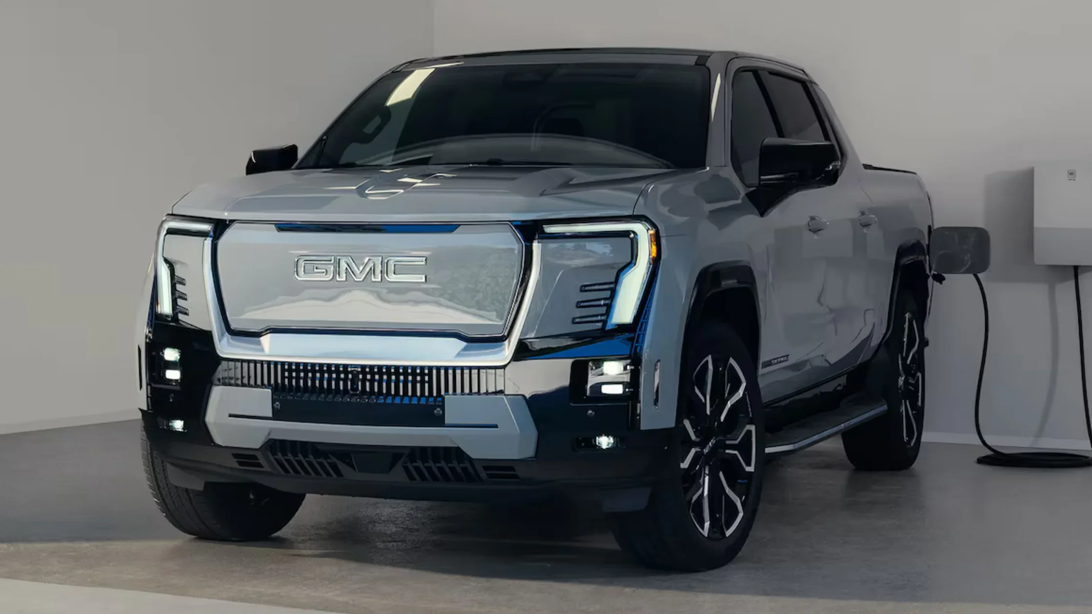 Front view of 2025 GMC Sierra EV Denali Edition 1 charging indoors with bold LED grille.