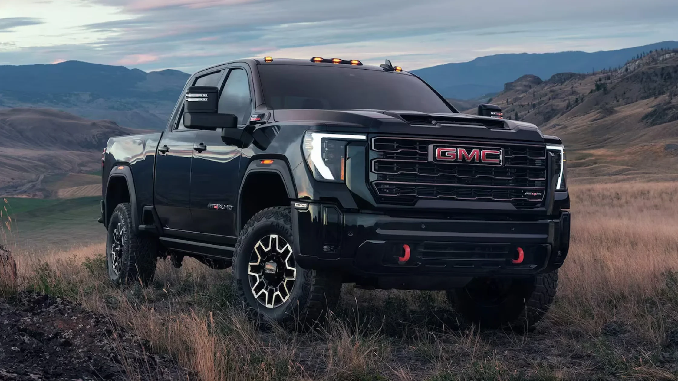 2025 GMC Sierra HD AT4X pickup truck parked on rugged mountain terrain at sunset