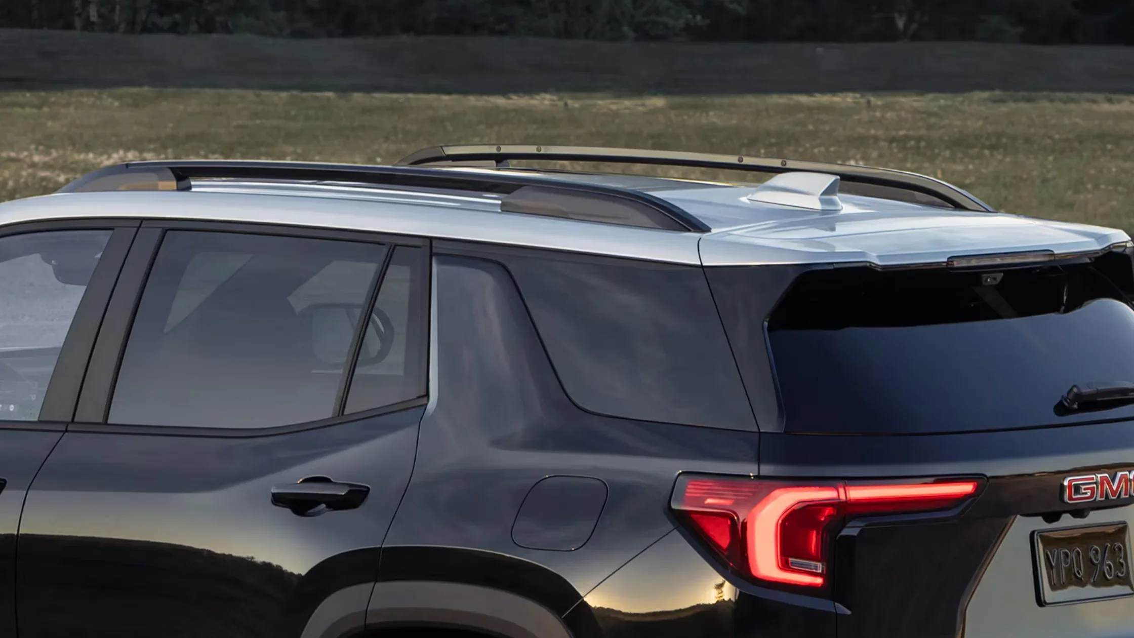 Rear-side angle of black 2025 GMC Terrain showing roof rails, tinted glass, and C-shaped LED lights.