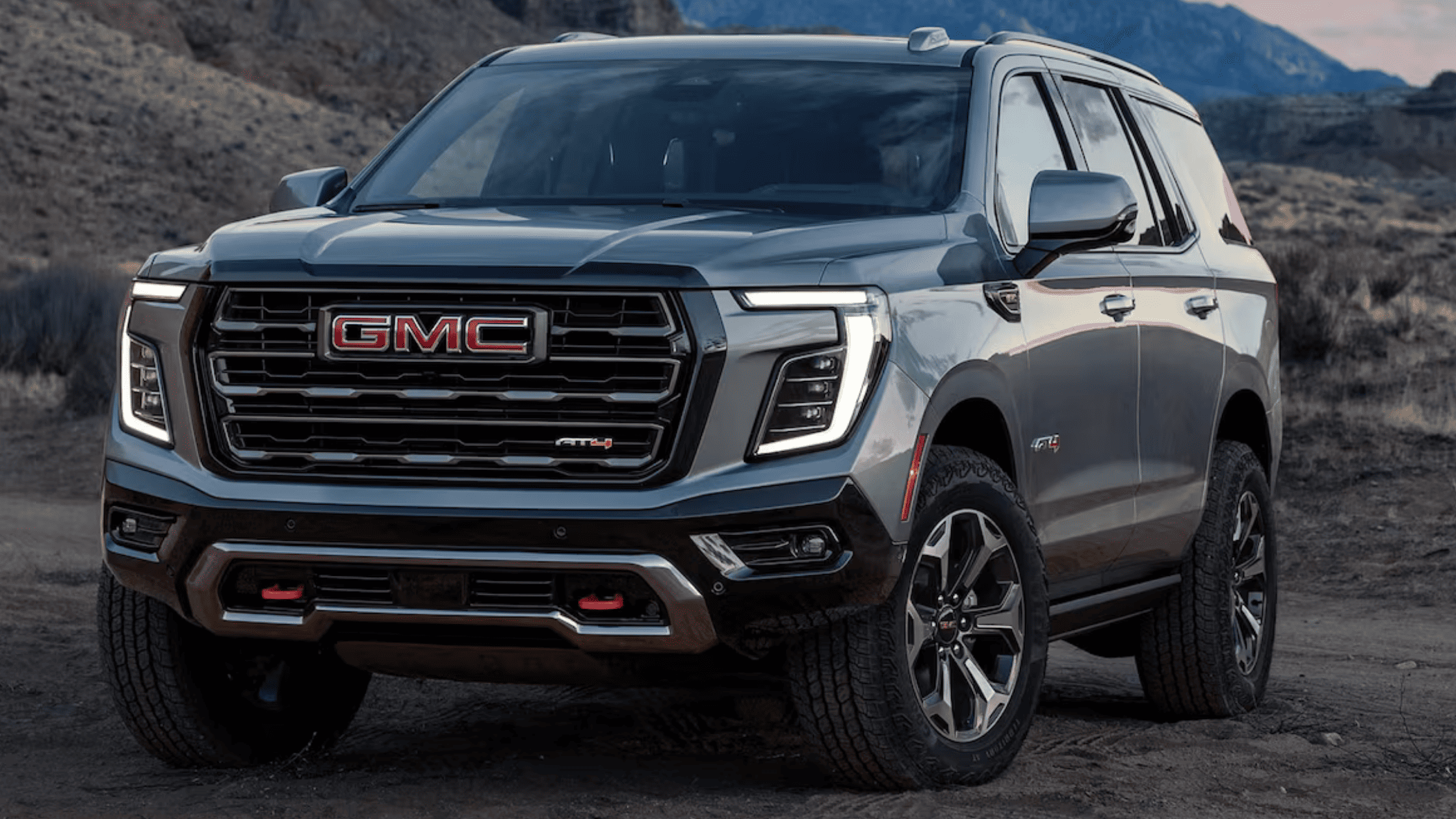 2025 GMC Yukon AT4 parked in desert terrain, highlighting rugged front grille and LED headlights.