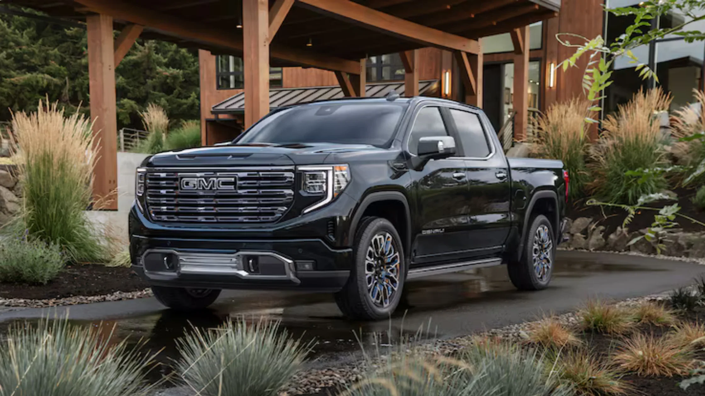 Front angle of 2026 GMC Sierra 1500 Denali parked in front of modern home with upscale landscaping.